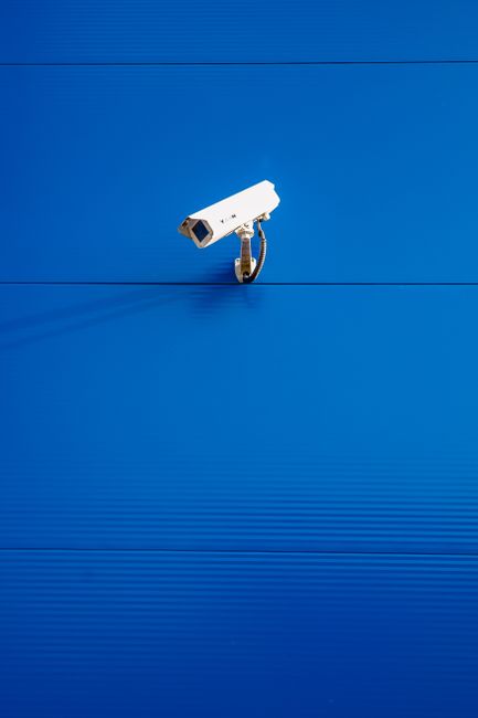 White security camera against a vibrant blue textured wall in a minimalist style.
