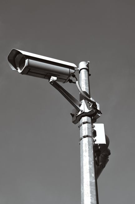 Black and white photo of a surveillance camera mounted on a pole against a clear sky in Zagreb, Croatia.